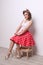 Pinup beautiful girl in red skirt poses on wooden stool