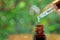 Pipette with essence drop and bottle, closeup on blurred nature background. Herbal essential massage oil dripping into