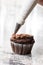 Piping bag with chocolate ganache cream above chocolate cup cake on the grey granite background