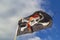 Pirate flag `Jolly Roger` on a background of blue sky with clouds on a bright sleepy day.