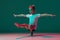 Pistol squat. Little flexible girl, rhythmic gymnastics artist training isolated on green studio background in neon pink