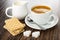 Pitcher with milk, wafers, cup with black coffee, spoon in saucer, pieces of sugar on wooden table