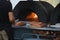 Pizza being cooked in woodfired pizza oven at outdoor party with generic unbranded pizza boxes