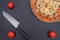 Pizza on a black background with a knife and ingredients.