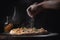 Pizza chef hand sprinkles salt on a pizza on a black background, In a close-up view, the hands of a chef skillfully assemble a