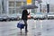 Pizza delivery man carries a pizza bag in right hand and umbrella in left hand.