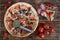 Pizza with pepperoni, salami, mushrooms and olives lies on a rustic table alongside red pepper, tomatoes, cheese, sausage and a