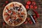 Pizza with pepperoni, salami, mushrooms and olives lies on a rustic table alongside red pepper, tomatoes and a special circular