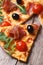 Pizza with prosciutto, tomatoes and arugula, olives closeup