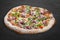 Pizza with roast beef and artichokes, jalapenos, chili, mozzarella, pesto. Neapolitan round pizza on dark background