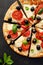 Pizza slices with tomatoes, mozzarella cheese, black olives and fresh basil on a black background, close-up, top view.