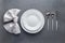 Place setting with white napkin, empty plate and silver cutlery on a gray concrete grunge table. Top view. Festive dinner in a