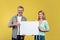 Place for your ad. Happy mature spouses holding empty blank placard board and man pointing at it, yellow background