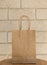 Plain blank brown paper bag in front of a beige brick background
