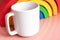 Plain blank white 11oz cup in front of a wooden toy rainbow on a pink shiny background