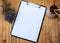 Plain Office Clipboard With Stack Of Pens In A Holder Beside A Flower Vase. Empty Paper Sheet With Colorful Pencils Next