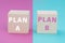 Plan A and B standing on wooden cubes, pink and blue colored background