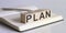 The PLAN sign on a wooden block on notebook background