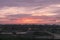 Plane against orange and purple sky at sunset, with misty mounds of earth and buildings against trees