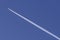 A plane crosses the blue sky diagonally leaving behind a long white trail