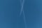 The plane flies through the clear blue sky with long vapor trails.