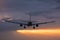 Plane flying towards the runway during a cloudy sunrise.