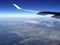 Plane wing with the blue sky and mainland covered with clouds