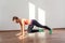 Plank with knee to elbow. Positive fit young woman with bun hairstyle and in tight sportswear smiling and practicing. indoor