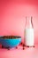 Plank milk in a glass bottle and chocolate breakfast cereals in a blue bowl on pink background