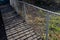 A plank walkway with stainless steel railings leads around the lake with rare ducks. the fence panel is made of rope fishing net.