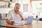 Planning, documents and finance with elderly man on laptop in a kitchen, reading retirement and savings plan in his home