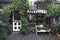 The plant-covered entrance to a small hidden and cozy shop. White door and window frames. An awning protects the window. in front