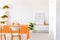 Plant next to cabinet with poster in white dining room interior with chairs at orange table