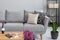 Plant next to grey settee with cushions in flat interior with flowers and wooden table