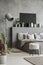 Plant, stool and lamp in modern grey bedroom interior with poster above bed. Real photo