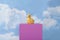 a plaster duck on a pink cube in front of a blue sky with clouds