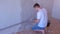 Plasterer man is aligning wet plaster on wall using long metal tool spatula.