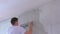 Plasterer man is aligning wet plaster on wall using long metal tool spatula.