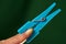 plastic blue clothes peg pinching hand index finger under green background