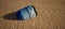 Plastic blue drum lying in rippled sand of beach.