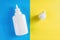 Plastic bottle and cap on blue and yellow background. Aerosol from common cold or allergy, spray for nose, medical drops