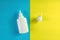 Plastic bottle and cap on blue and yellow background. Aerosol from common cold or allergy, spray for nose, medical drops