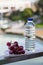 Plastic bottle with drinking water, next to the ripe grapes on a saucer against the background of nature and water