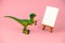 plastic dinosaur toy holding artistic brush and standing near mock up canvas, creative conceptual still life on a pink