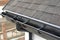 Plastic guard brush in grey plastic rain gutter on asphalt shingles roof.