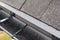 Plastic guard brush in grey plastic rain gutter on asphalt shingles roof.