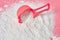 Plastic measuring spoon on heap of washing powder for cleaning clothes lies on pink countertop in laundry