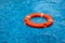 Plastic orange lifebuoy on blue water of swimming pool. Safety on water concept. Kids swimming lesson equipment