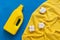 Plastic packaging of liquid washing powder, a yellow terry towel and cotton flowers on a blue painted background. Eco cleaning