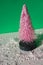 Plastic pink Christmas tree isolated on a green surface with fake snow.  New Year's concept and background.